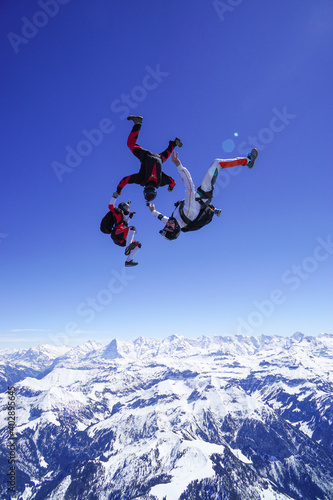 Skydivers perform stunts above snowcapped mountains