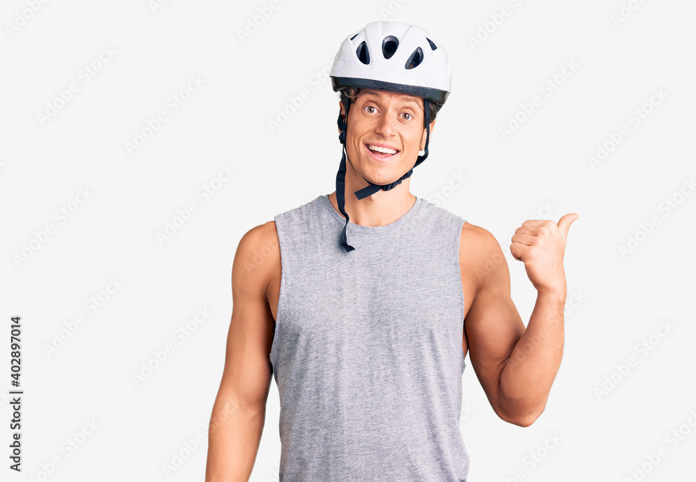 Young handsome man wearing bike helmet smiling with happy face looking and pointing to the side with thumb up. Young handsome man wearing bike helmet smiling with happy face looking and pointing to the side with thumb up.