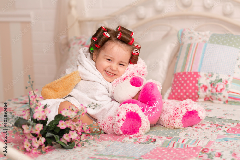 Adorable little girl with hair curlers hugs her favorite teddy bear toy Adorable little girl with hair curlers hugs her favorite teddy bear toy