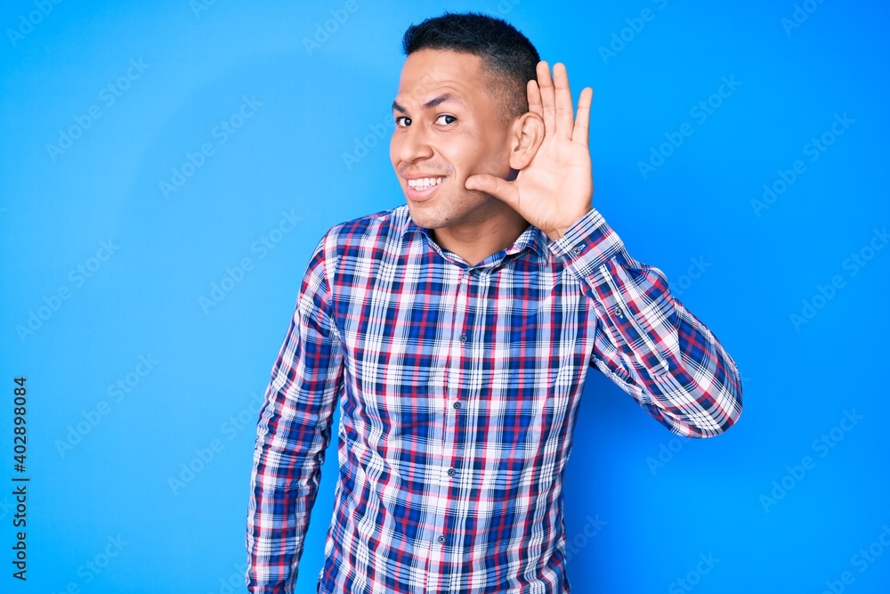 Young handsome latin man wearing casual clothes smiling with hand over ear listening an hearing to rumor or gossip. deafness concept. Young handsome latin man wearing casual clothes smiling with hand over ear listening an hearing to rumor or gossip. deafness concept.