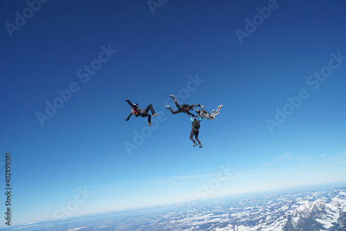 Skydivers perform stunts above snowcapped mountains