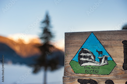 Obraz na płótnie Padina, Romania - January 2021: Winter landscape with a wooden sign of the Bucegi Natural Park, pine forest and mountain peaks in the background on a sunny morning. w salonie