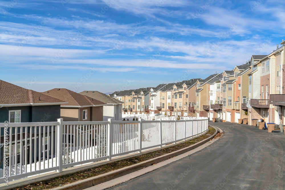Townhouses along road with white fence against scenic blue sky and white clouds