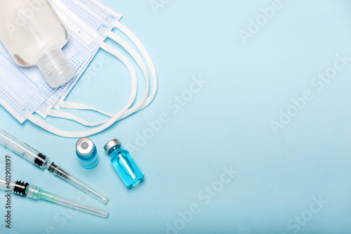 Medical bottle, hand sanitizer, vials, syringes and face mask on blue background with copy space. Vaccination session and immunity improvement.