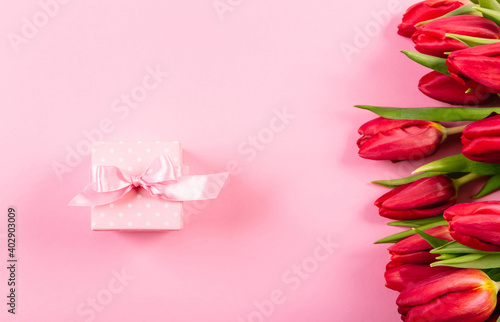 Gift box with a pink ribbon in white polka dots on a background of a bouquet of red tulips with copy space for text. Wallpaper or banner for gift shop, flower shop or jewelry store. Valentine day
