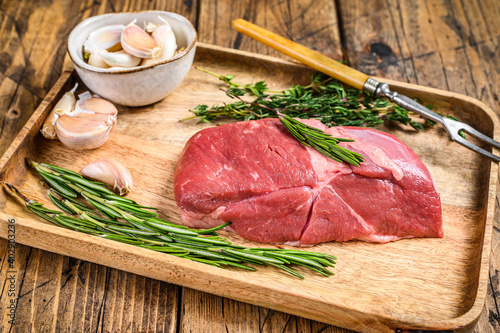 Raw lamb meat steak in a wooden tray with herbs. wooden background. Top view