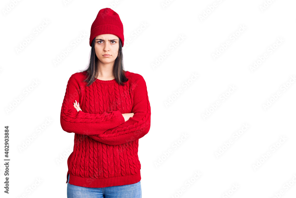 Young beautiful girl wearing sweater and wool cap skeptic and nervous, disapproving expression on face with crossed arms. negative person. Young beautiful girl wearing sweater and wool cap skeptic and nervous, disapproving expression on face with crossed arms. negative person.