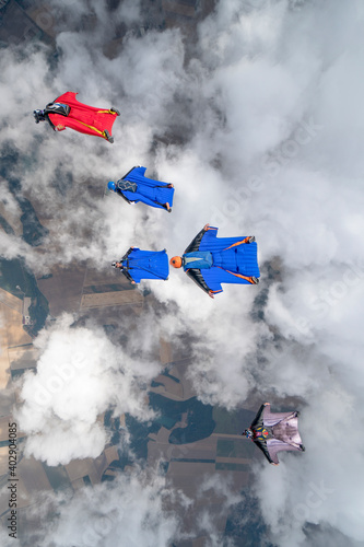 Team of wingsuit fliers glide in formation at sunset