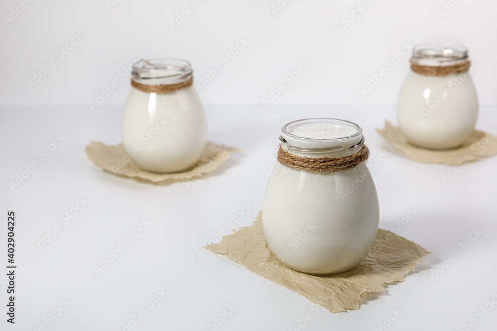 Yogurt in glass jars on a paper base and white background.