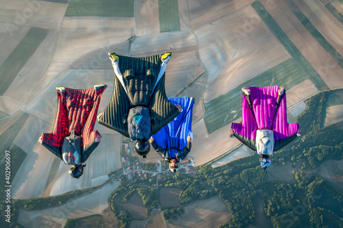Team of wingsuit fliers glide in formation at sunset