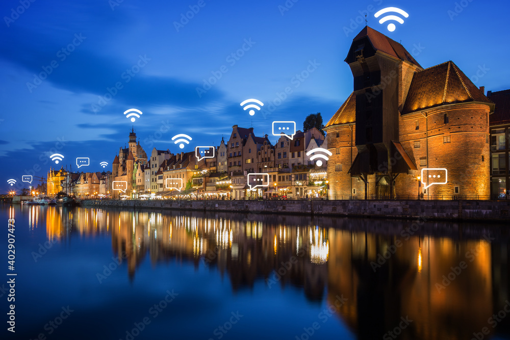Lit Crane and other old buildings along the Long Bridge waterfront at the Main Town in Gdansk, Poland, at dusk. Wireless network connection, WiFi, smart city and online messaging concept.