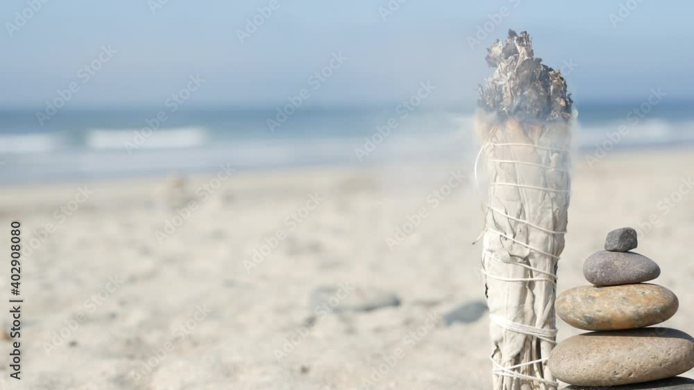 Dried white sage smoke, smudge stick burning in soft focus with bokeh, aroma smudging close up. Rock balancing on ocean beach, stones stacking by sea water waves. Zen pyramid of pebbles on sandy shore Dried white sage smoke, smudge stick burning in soft focus with bokeh, aroma smudging close up. Rock balancing on ocean beach, stones stacking by sea water waves. Zen pyramid of pebbles on sandy shore