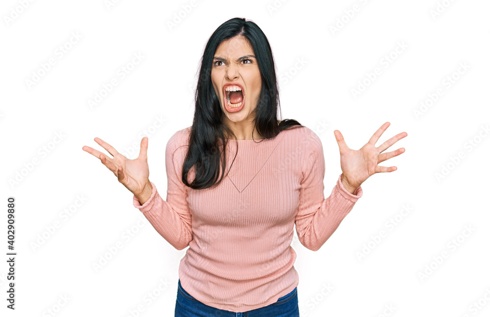 Young hispanic woman wearing casual clothes crazy and mad shouting and yelling with aggressive expression and arms raised. frustration concept. Young hispanic woman wearing casual clothes crazy and mad shouting and yelling with aggressive expression and arms raised. frustration concept.