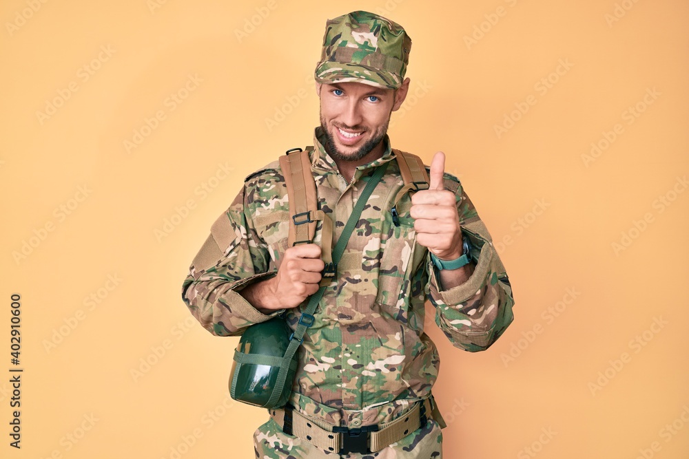 Young caucasian man wearing camouflage army uniform and canteen smiling happy and positive, thumb up doing excellent and approval sign Young caucasian man wearing camouflage army uniform and canteen smiling happy and positive, thumb up doing excellent and approval sign