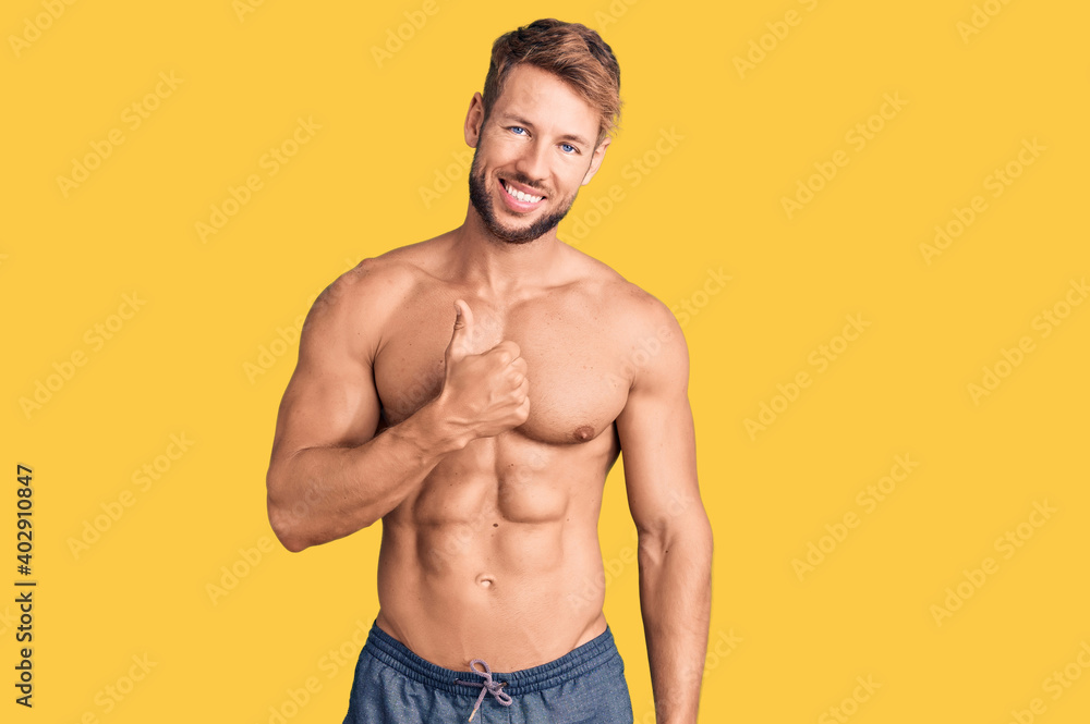 Fototapeta premium Young caucasian man standing shirtless doing happy thumbs up gesture with hand. approving expression looking at the camera showing success.