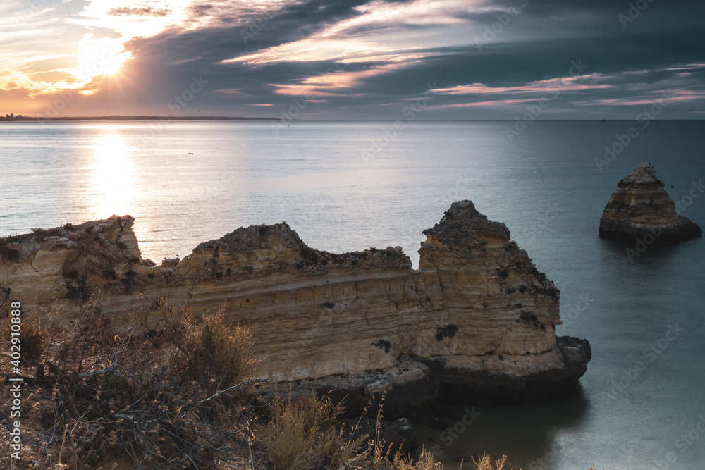 Landscape photo. Scenic rocks by the coast, still water and warm sky at dusk. Lagos, Algarve Coast, Portugal