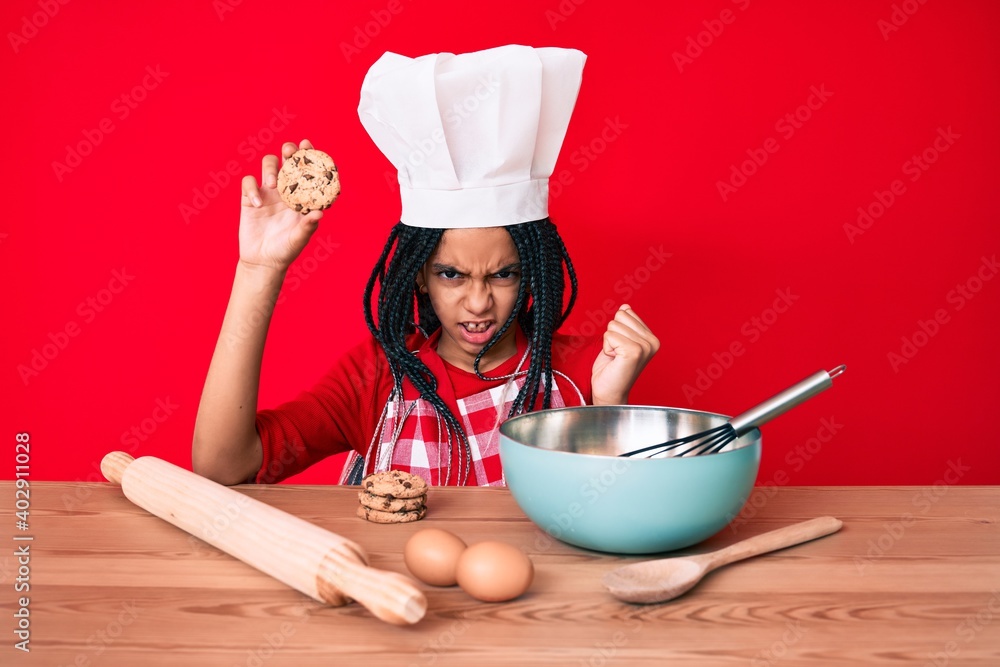 Young african american girl child with braids wearing professional baker apron holding cookie annoyed and frustrated shouting with anger, yelling crazy with anger and hand raised Young african american girl child with braids wearing professional baker apron holding cookie annoyed and frustrated shouting with anger, yelling crazy with anger and hand raised