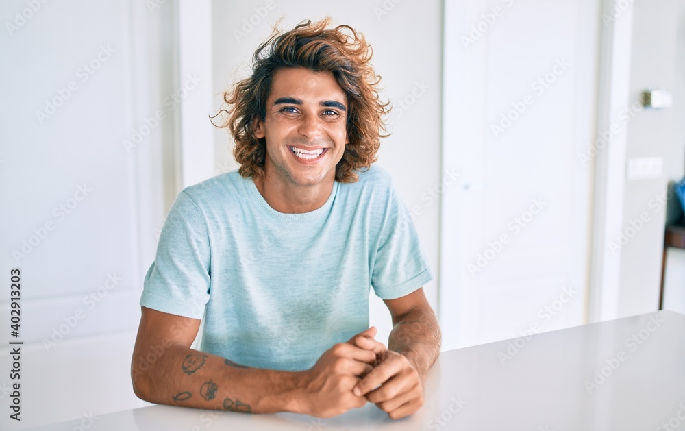 Young hispanic man smiling happy sitting on the table at home Young hispanic man smiling happy sitting on the table at home