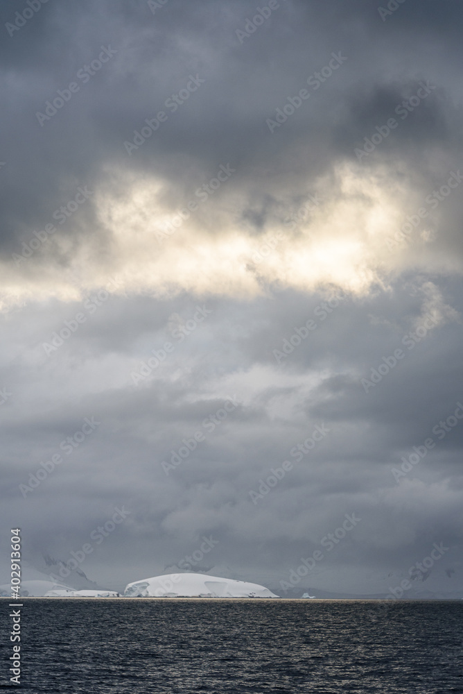 Rocky frozen landscape with stormy gray skies with some clouds highlighted white by the sun, Southern Ocean, Antarctica
