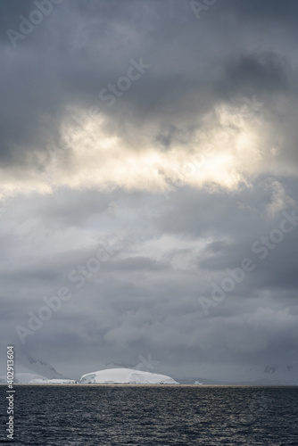 Rocky frozen landscape with stormy gray skies with some clouds highlighted white by the sun, Southern Ocean, Antarctica 