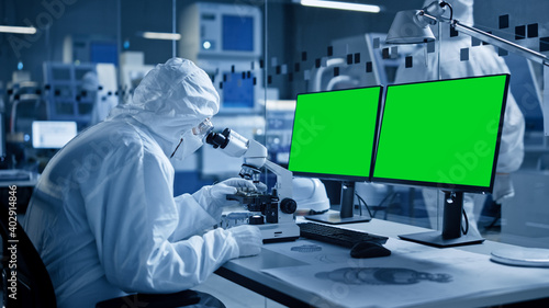 Research Factory Cleanroom: Close-up of Engineer / Scientist wearing Coverall and Gloves Uses Microscope, Computer Shows Chroma Key Green Screen Display. Scientific and Electronics Research Facility
