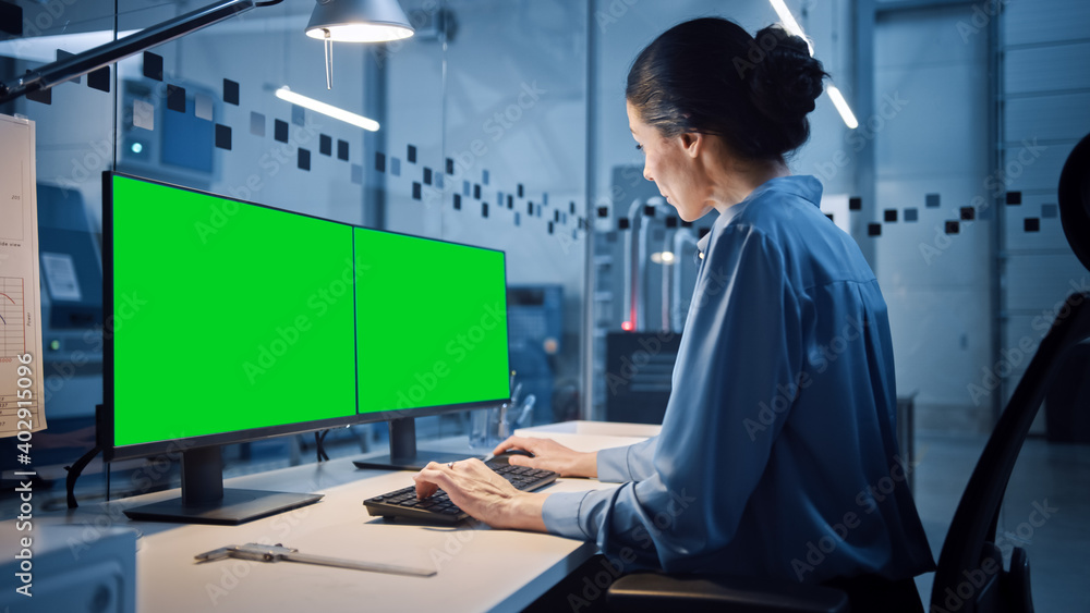 Factory Office: Portrait of Beautiful and Confident Female Industrial Engineer Working on Personal Computer with Two Green Screen Chroma Key Displays. High Tech Facility with CNC Machinery