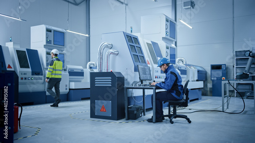 In Factory: Professionals Working on CNC Machinery, Walk Through Workshop, Use Computers, Manipulate Robot Arm Production Line. Engineer Controls System with Computer.