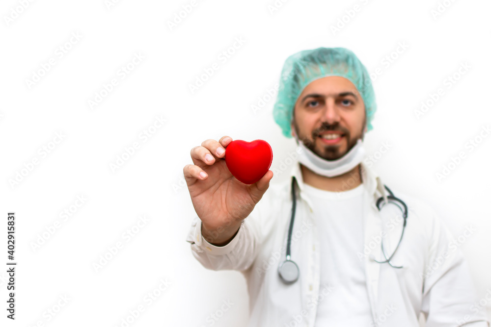 Portrait of male doctor in white coat wearing white mask and holding heart sign. Stethoscope on the neck. Isolated on white background. Healthcare And Medicine. Heart disease prevention concept. Portrait of male doctor in white coat wearing white mask and holding heart sign. Stethoscope on the neck. Isolated on white background. Healthcare And Medicine. Heart disease prevention concept.