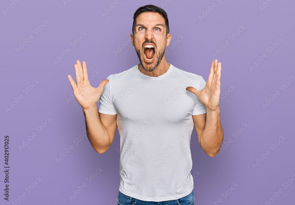 Handsome man with beard wearing casual white t shirt crazy and mad shouting and yelling with aggressive expression and arms raised. frustration concept. Handsome man with beard wearing casual white t shirt crazy and mad shouting and yelling with aggressive expression and arms raised. frustration concept.