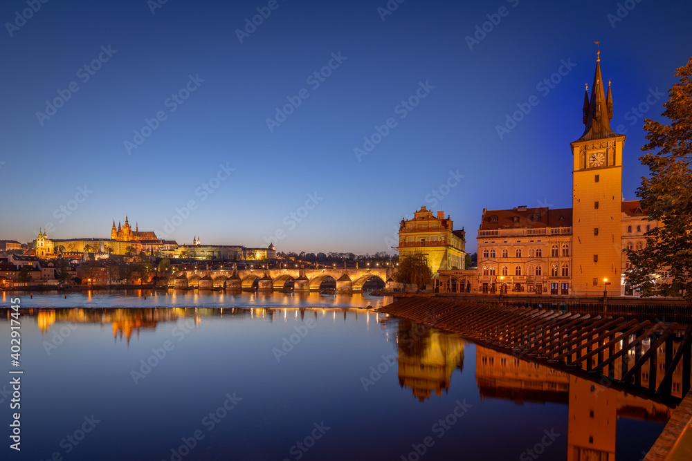 View on Charles Bridge and Prague Castle over Vltava River during early night with wonderful blue sky and yellow city lights, Czechia, Europe