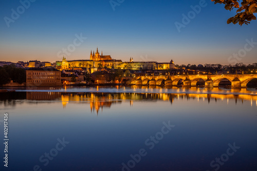 View on Charles Bridge and Prague Castle over Vltava River during early night with wonderful blue sky and yellow city lights, Czechia, Europe