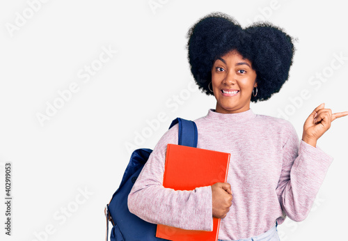 Young african american girl wearing student backpack holding book smiling happy pointing with hand and finger to the side