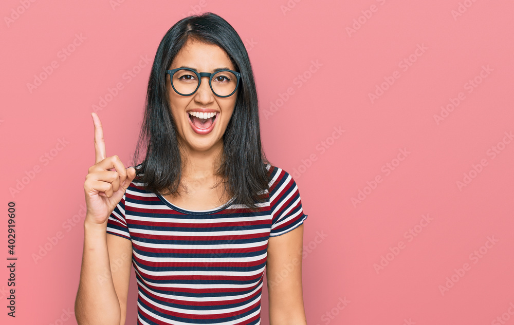Beautiful asian young woman wearing casual clothes and glasses pointing finger up with successful idea. exited and happy. number one. Beautiful asian young woman wearing casual clothes and glasses pointing finger up with successful idea. exited and happy. number one.