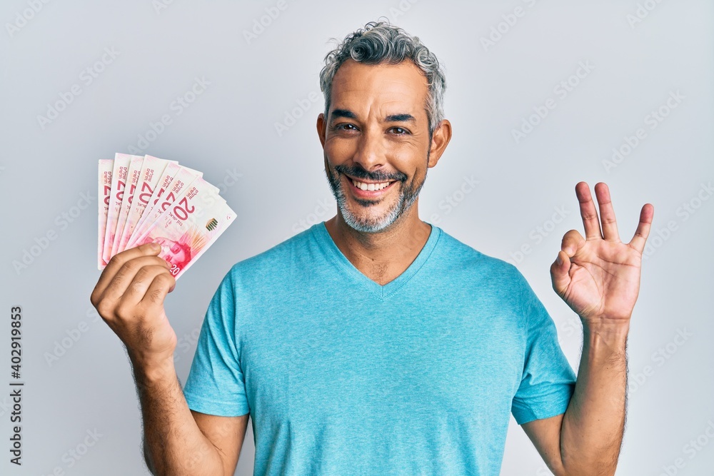 Middle age grey-haired man holding israel shekels doing ok sign with fingers, smiling friendly gesturing excellent symbol Middle age grey-haired man holding israel shekels doing ok sign with fingers, smiling friendly gesturing excellent symbol