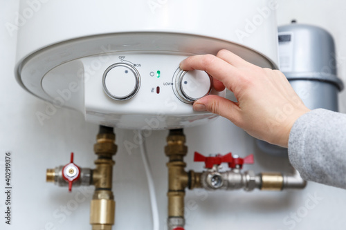 фотографія Female hand puts thermostat of electric water heater (boiler) in low low power consumption mode