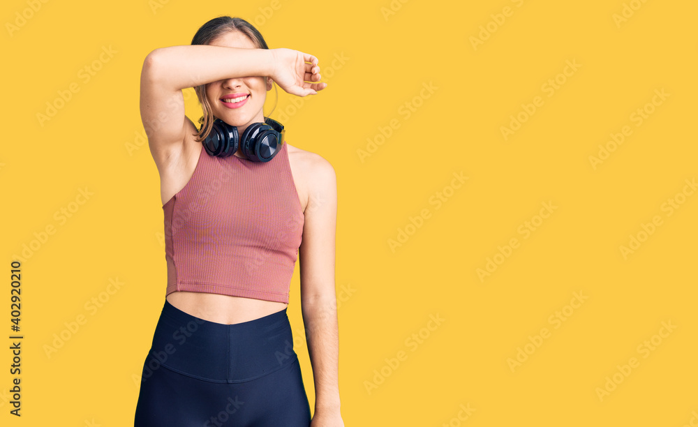 Beautiful caucasian young woman wearing gym clothes and using headphones covering eyes with arm smiling cheerful and funny. blind concept. Beautiful caucasian young woman wearing gym clothes and using headphones covering eyes with arm smiling cheerful and funny. blind concept.