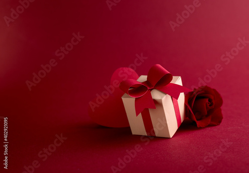 Happy st. Valentines day concept with craft paper gift box, red paper hearts and fresh rose against dark red background with space for text.