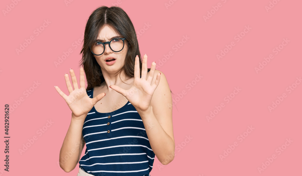 Young beautiful caucasian girl wearing casual clothes and glasses afraid and terrified with fear expression stop gesture with hands, shouting in shock. panic concept. Young beautiful caucasian girl wearing casual clothes and glasses afraid and terrified with fear expression stop gesture with hands, shouting in shock. panic concept.