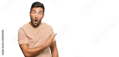 Handsome hispanic man wearing casual clothes surprised pointing with finger to the side, open mouth amazed expression.