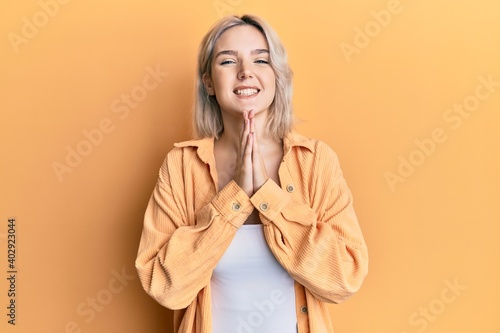 Young blonde girl wearing casual clothes praying with hands together asking for forgiveness smiling confident.