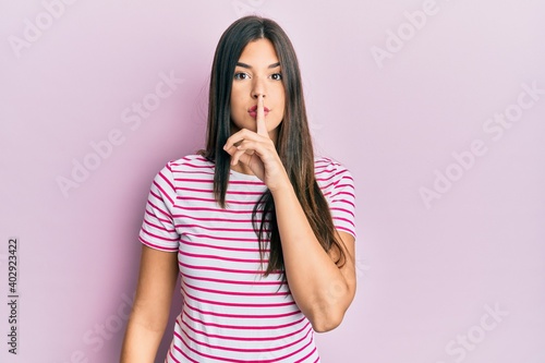 Young brunette woman wearing casual clothes over pink background asking to be quiet with finger on lips. silence and secret concept.