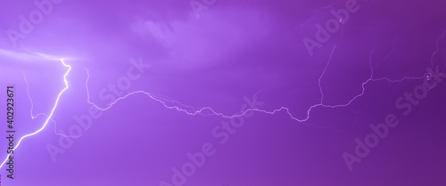 Panoramic photo of electric discharge from a stormy sky with lightning activity. Sky in purple (magenta) color.