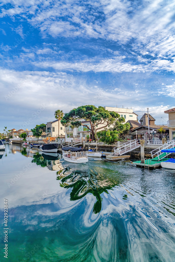 Clear water reflecting clouds and blue sky bordered by homes in Huntington Beach