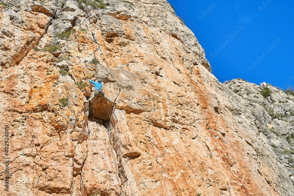 Horizontal low angle photo of a climber climbing a reddish mountain, with blue sky on a sunny day Horizontal low angle photo of a climber climbing a reddish mountain, with blue sky on a sunny day