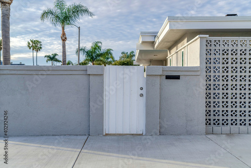 White gate and concrete fence agaonst trees and cloudy sky of beautiful home
