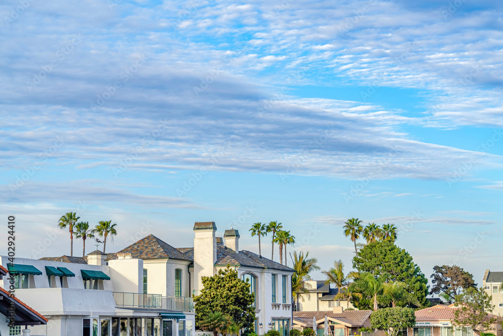 Charming homes and lush green trees with pale blue sky and gray clouds overhead Charming homes and lush green trees with pale blue sky and gray clouds overhead