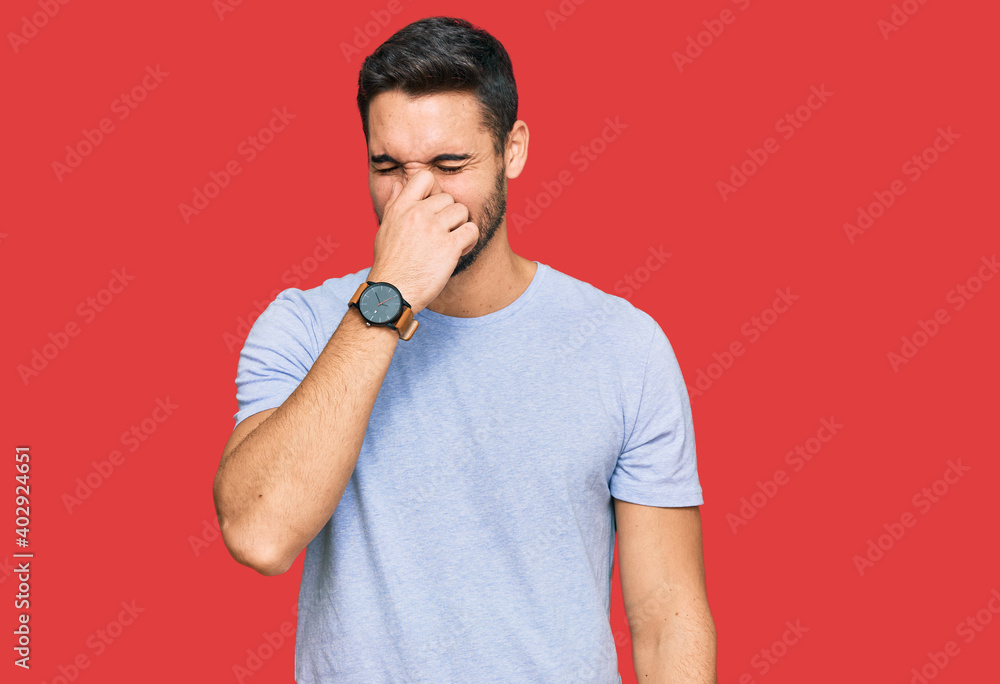 Young hispanic man wearing casual clothes smelling something stinky and disgusting, intolerable smell, holding breath with fingers on nose. bad smell Young hispanic man wearing casual clothes smelling something stinky and disgusting, intolerable smell, holding breath with fingers on nose. bad smell