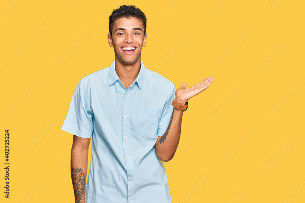 Young handsome african american man wearing casual clothes smiling cheerful presenting and pointing with palm of hand looking at the camera. Young handsome african american man wearing casual clothes smiling cheerful presenting and pointing with palm of hand looking at the camera.