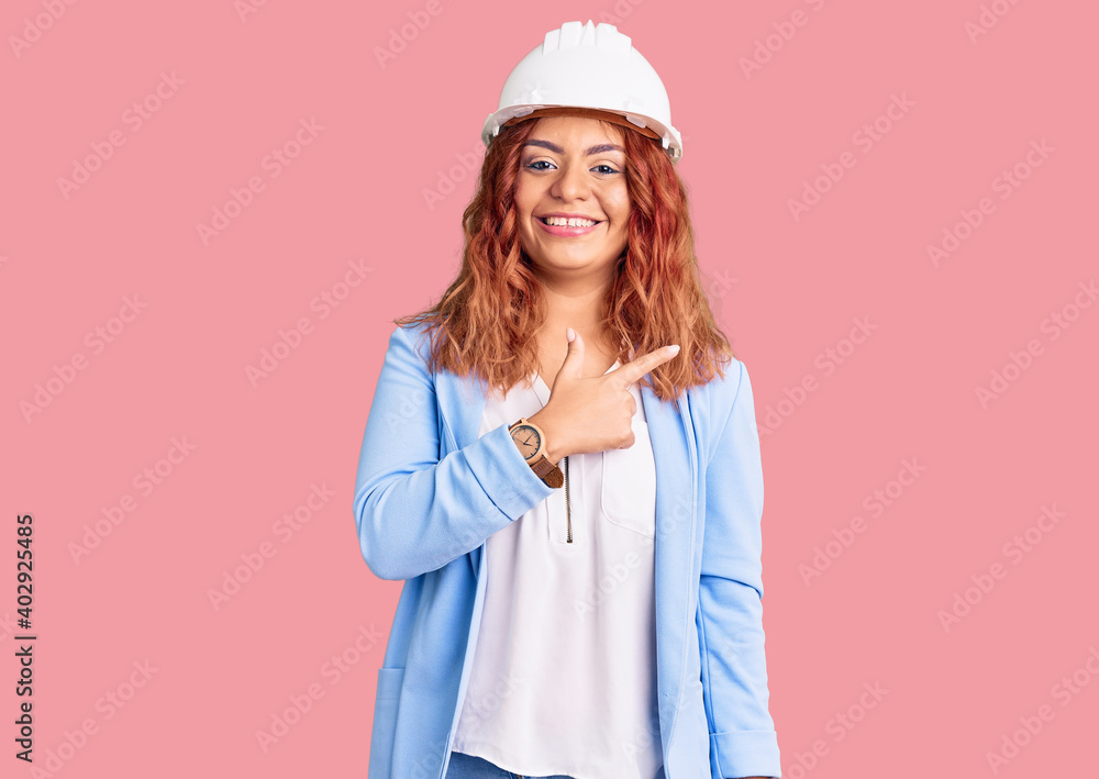 Young latin woman wearing architect hardhat cheerful with a smile of face pointing with hand and finger up to the side with happy and natural expression on face Young latin woman wearing architect hardhat cheerful with a smile of face pointing with hand and finger up to the side with happy and natural expression on face