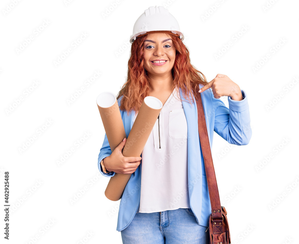 Young latin woman wearing architect hardhat holding blueprints pointing finger to one self smiling happy and proud Young latin woman wearing architect hardhat holding blueprints pointing finger to one self smiling happy and proud
